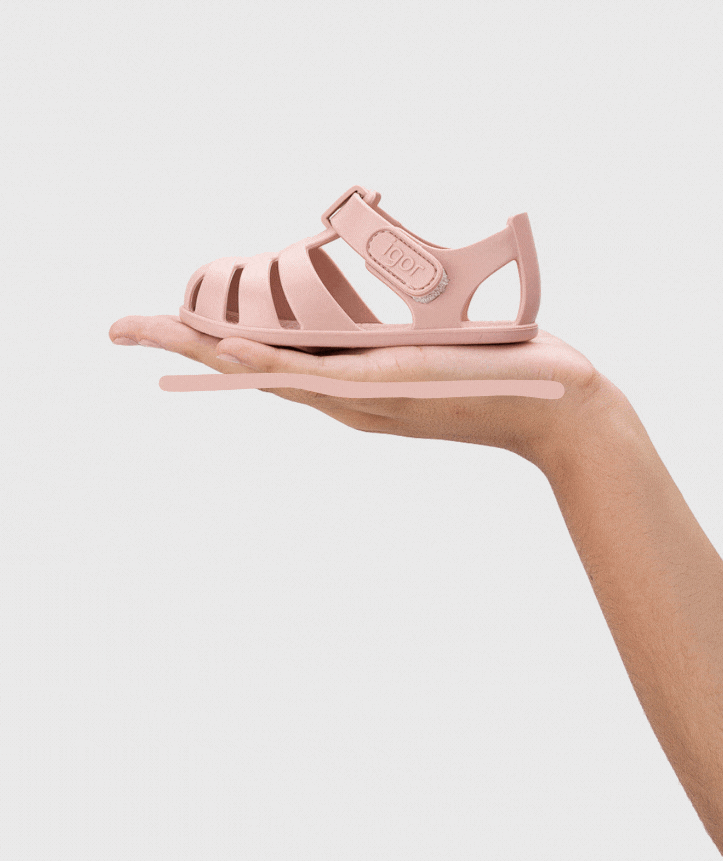 Sandália infantil rosa claro com fecho de velcro segurada numa mão