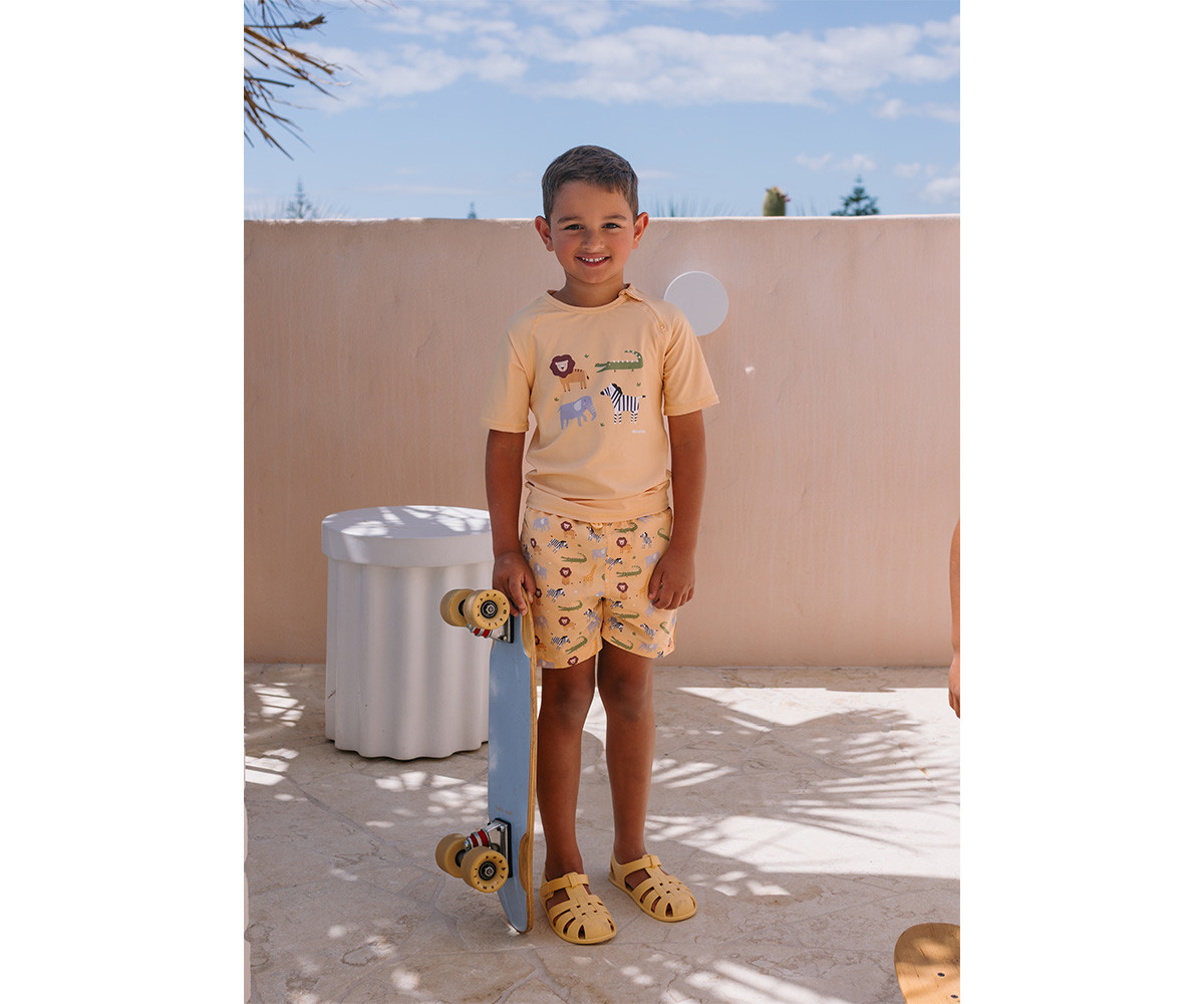 Menino com fato de banho bege claro e skate azul no terraço