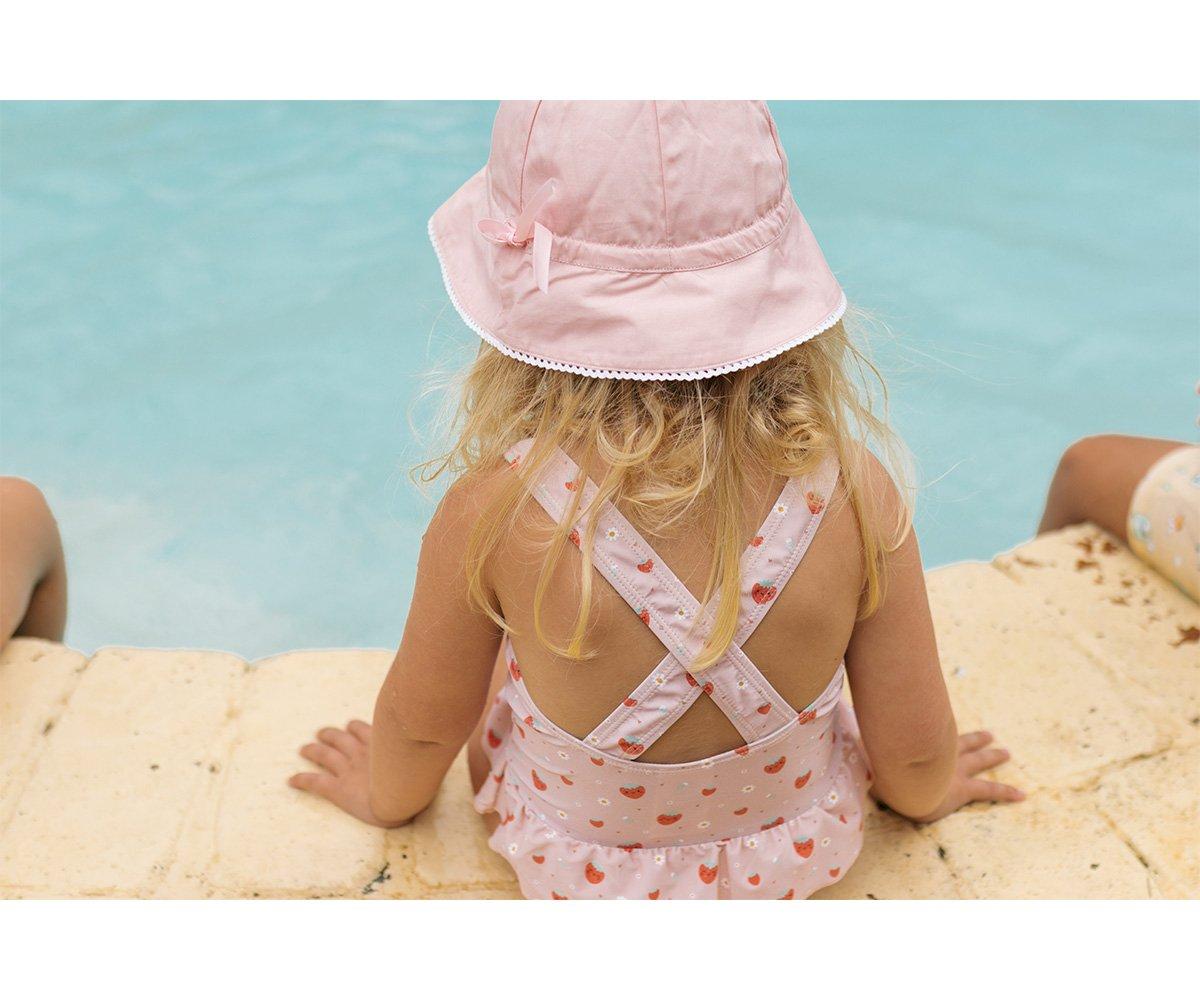 Criança de costas com vestido de banho rosa e chapéu rosa junto à piscina