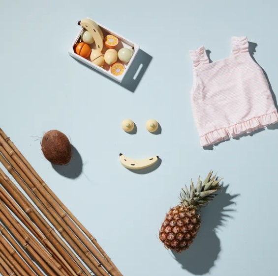 Blusa rosa infantil, brinquedos de madeira vegetarianos, cacho de bambu, coco, abacaxi e peças de madeira formando um rosto