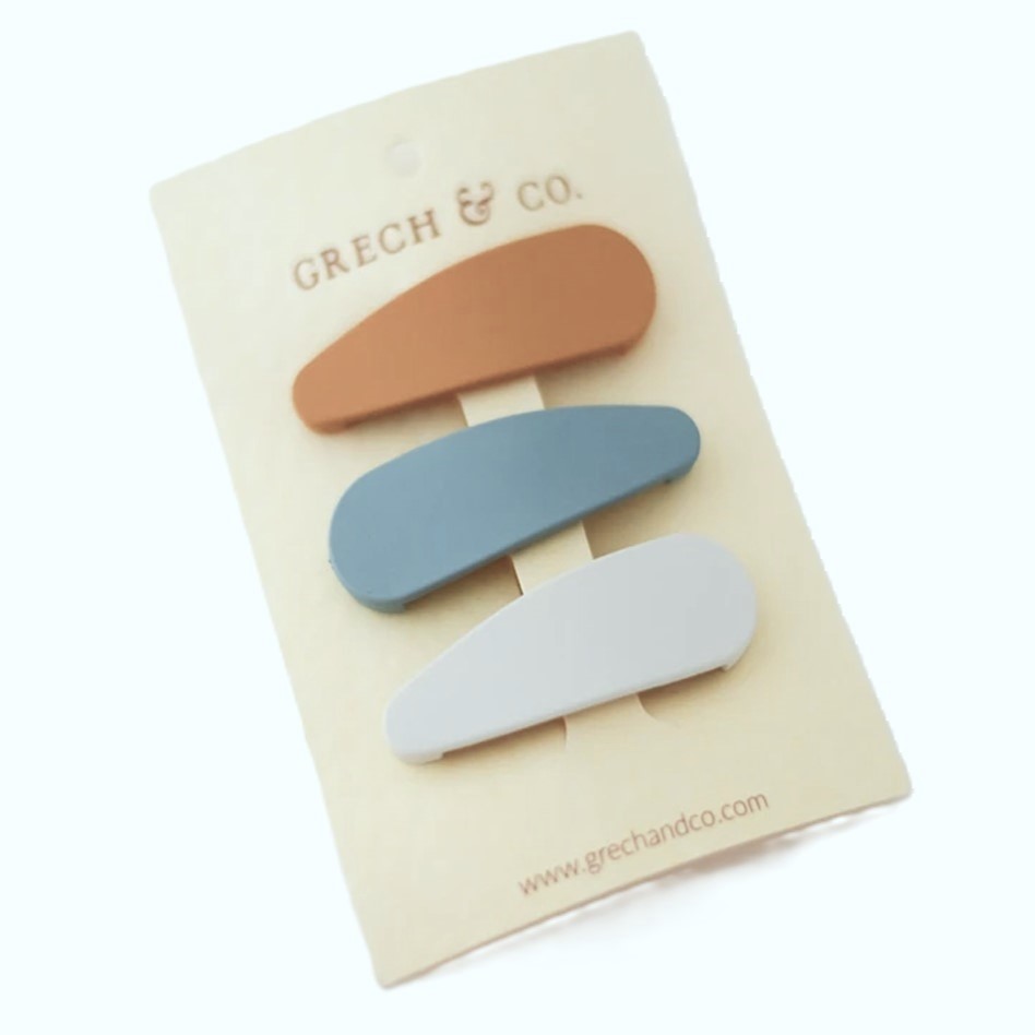 Três ganchos de cabelo em cartão branco com texto GRECH & CO.