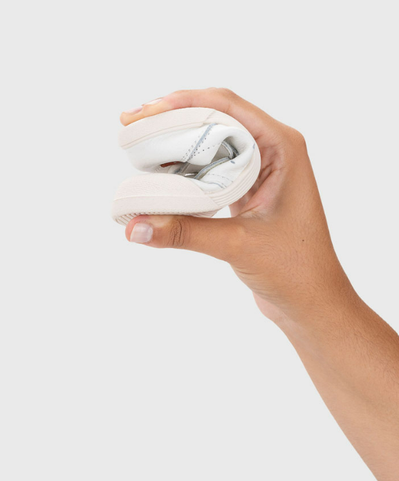 Ténis branco dobrado ao meio em mão sobre fundo branco