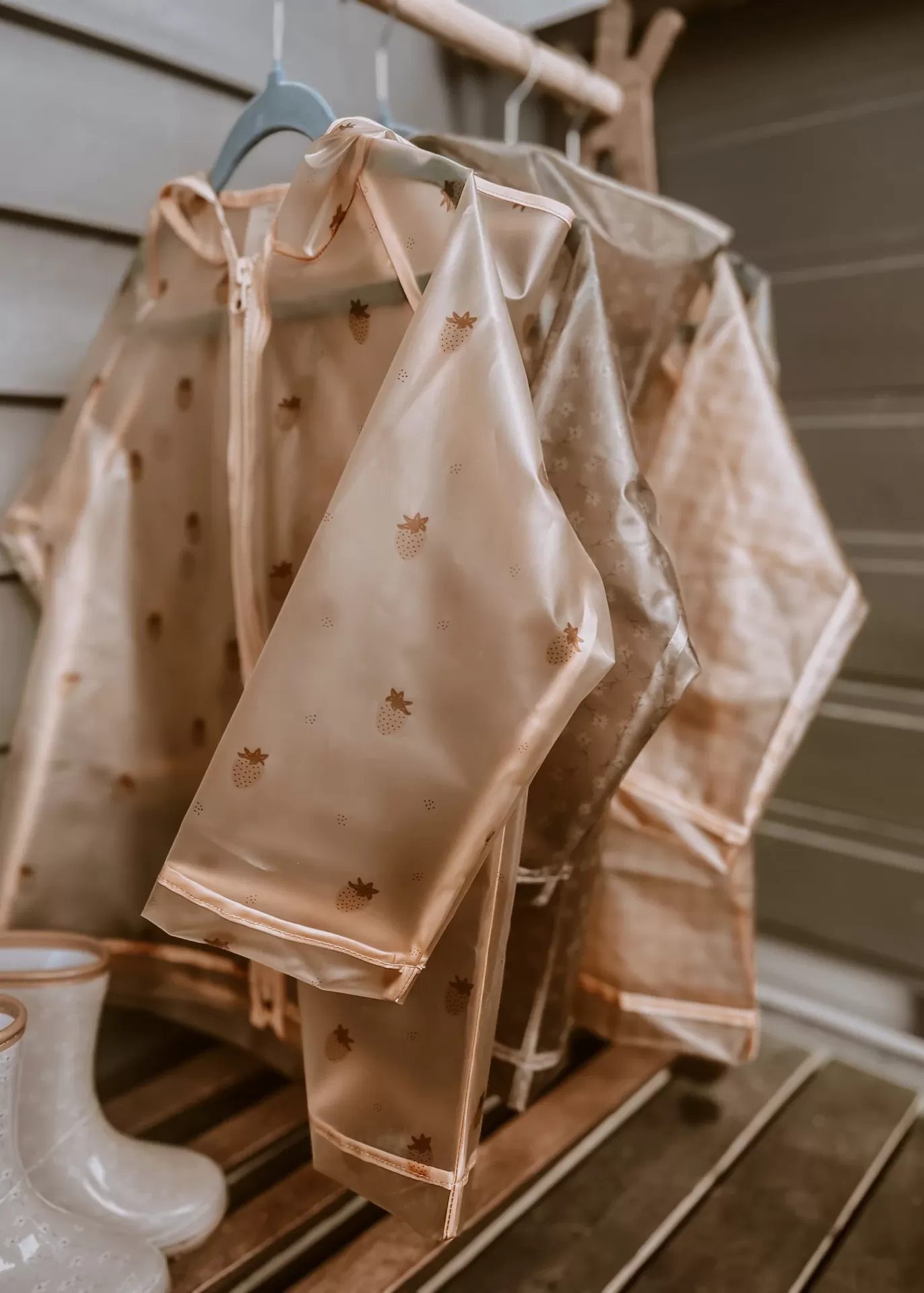 Macacões impermeáveis de criança bege com padrão castanho suspensos em cabides azuis em ambiente de madeira