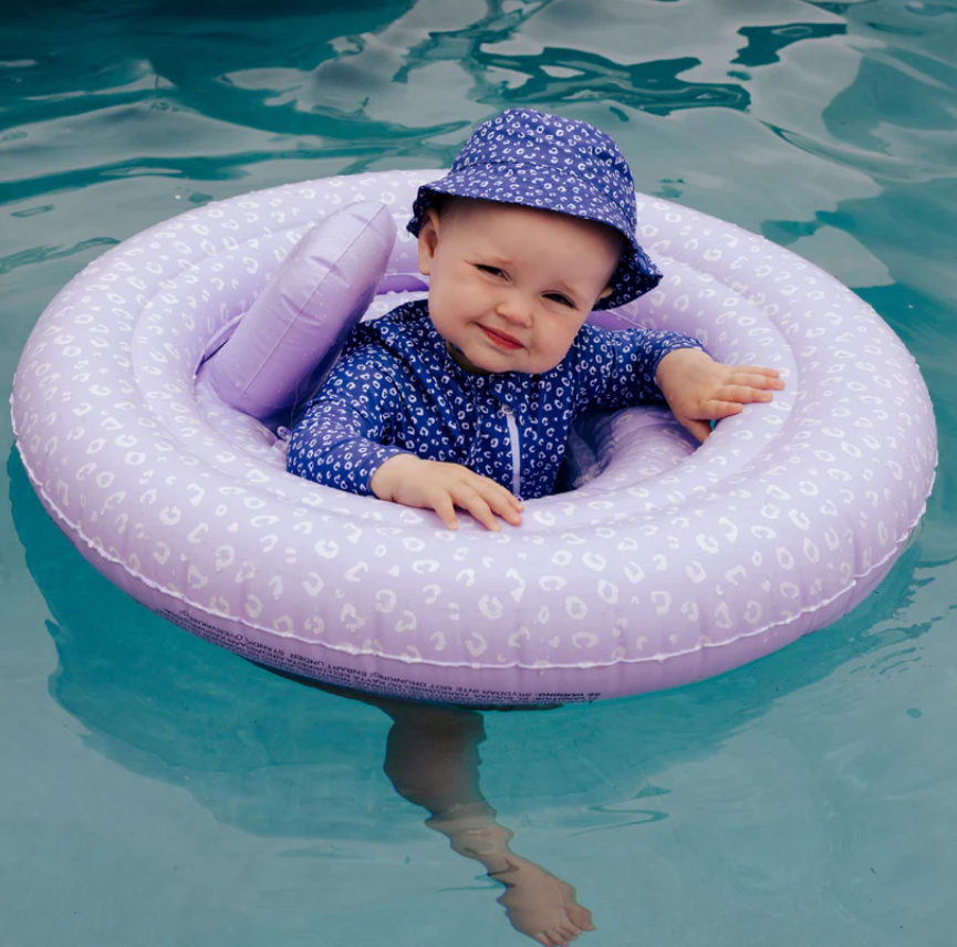 Bebé numa piscina sentado num anel insuflável lilás com chapéu azul