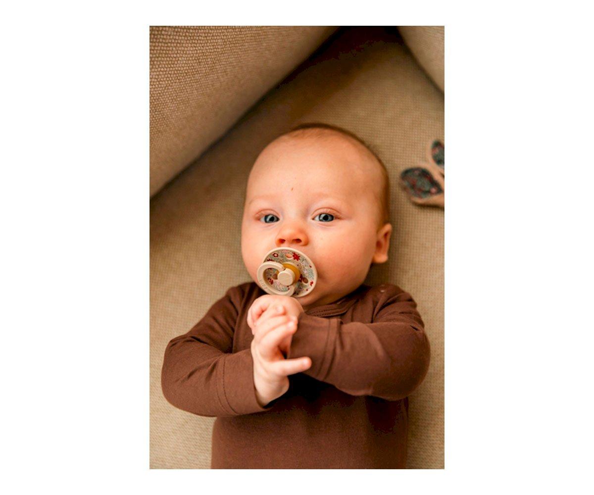 Bebé deitado com chupeta num sofá castanho claro