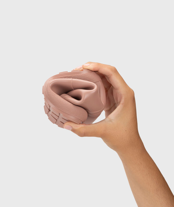 Sapato rosa claro flexível dobrado na mão, fundo cinza claro