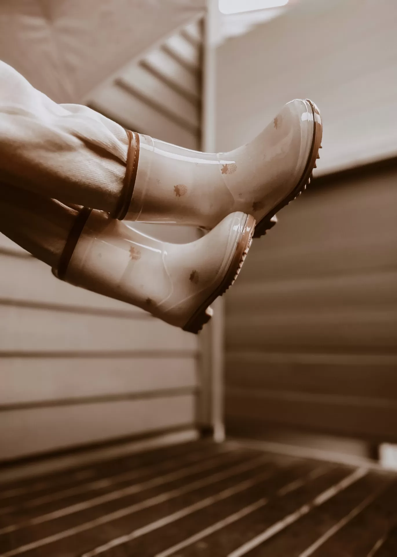 Botas de água bege com detalhes castanhos em ambiente interior com paredes de madeira