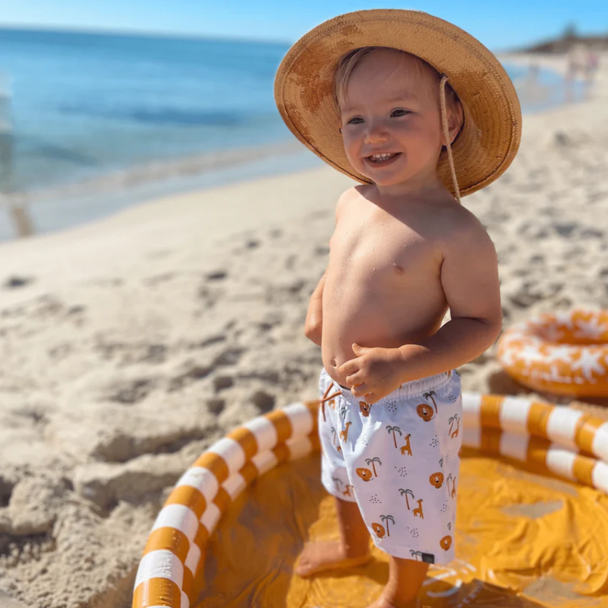Menino de chapéu de palha e calção branco com padrões dentro de piscina insuflável na praia