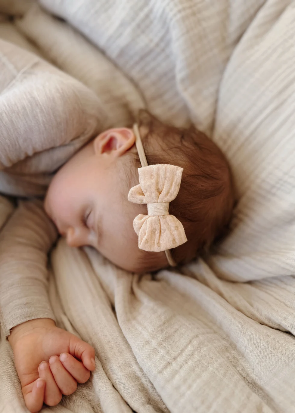 Bebé dormindo com faixa de cabelo bege com laço e roupa bege