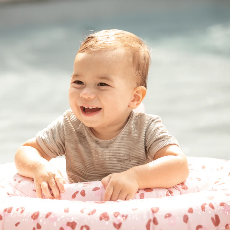 Bebé dentro de boia inflável cor-de-rosa com padrão de manchas vermelhas e brancas na água