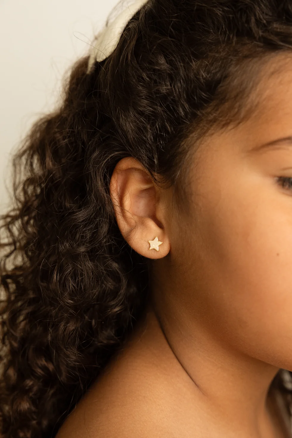 Brinco estrela dourado em orelha de mulher com cabelo encaracolado