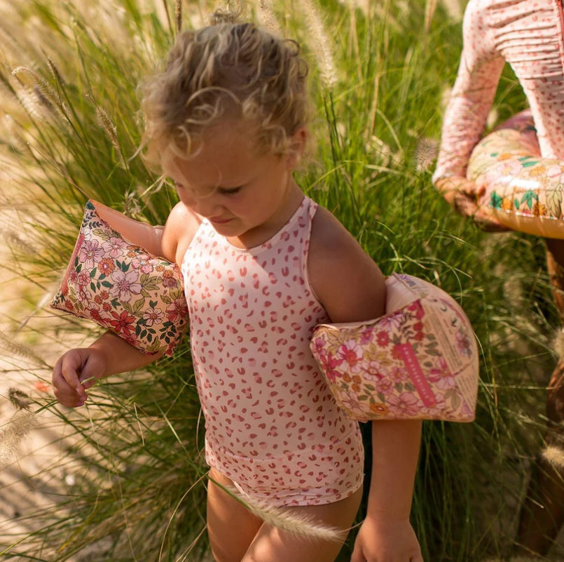 Criança com fato de banho rosa e braçadeiras florais junto a vegetação