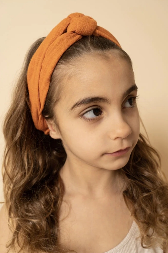 Criança com faixa de cabelo laranja com nó decorativo