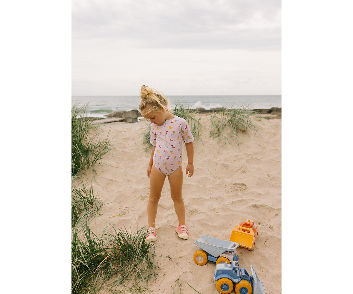 Criança na praia com fato de banho rosa claro e brinquedos na areia