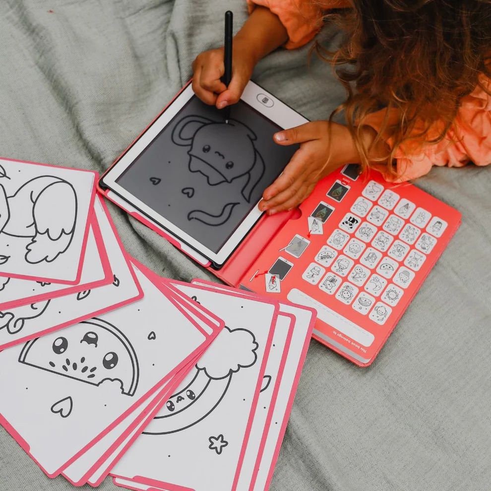 Criança a desenhar numa tablet com cartas de desenhos ao lado