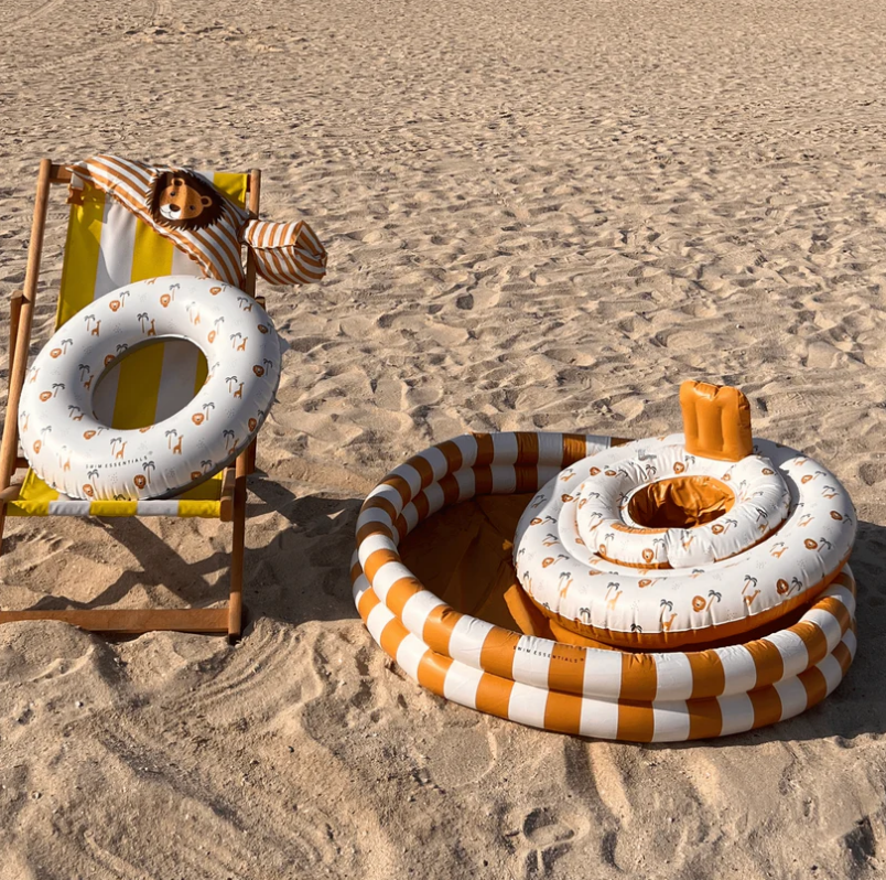 Brinquedos infláveis praia/piscina laranja e branco em areia, com espreguiçadeira de madeira e tecido riscado.