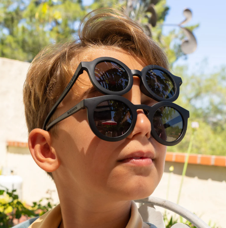 Criança usa dois pares de óculos de sol pretos ao ar livre