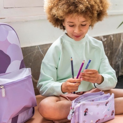 Criança com mochila e estojo lilás segurando lápis de cor, em ambiente interior