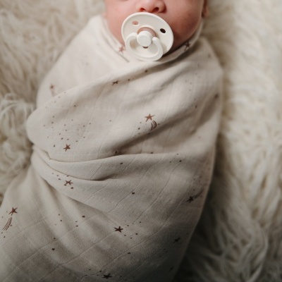 Bebé enrolado em manta branca com padrão de estrelas e chupeta