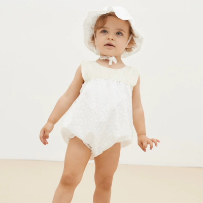 Bebé com macacão branco e chapéu branco de tecido leve