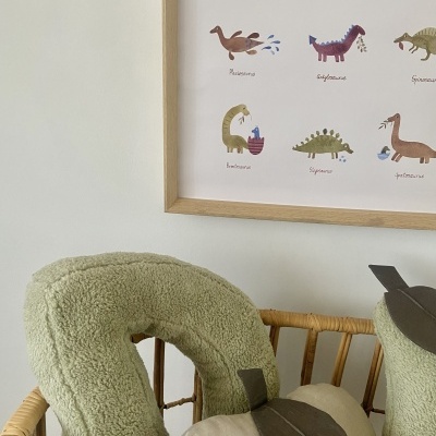 Almofadas verdes e bege em cadeira de madeira com poster de dinossauros na parede