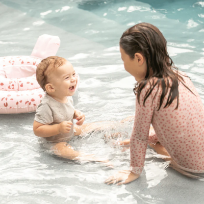 Bebé e criança na água com roupas de banho cor-de-rosa e cinzento e insuflável rosa