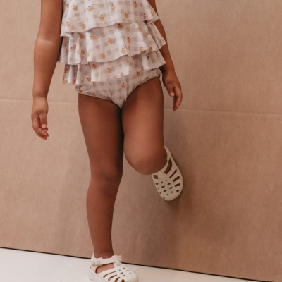 Fato de banho para criança com folhos e sapatos brancos.