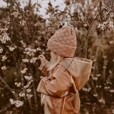 Criança com capa de chuva castanha e gorro de malha em ambiente natural outonal