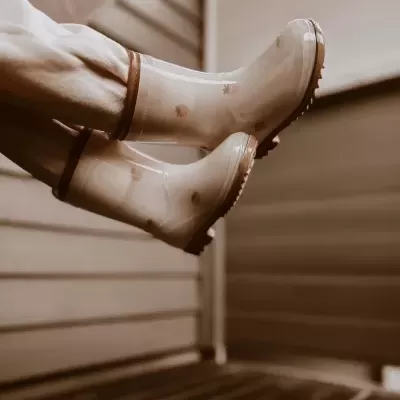 Botas de água bege com detalhes castanhos em ambiente interior com paredes de madeira