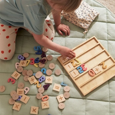 Criança a brincar com jogo educativo de madeira com números e símbolos coloridos num tapete verde claro