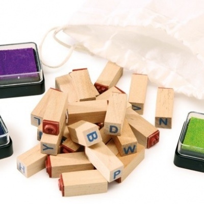 Carimbos de madeira com letras e almofadas de tinta coloridas junto a um saco branco