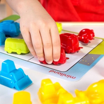 Criança a segurar carro de brinquedo vermelho com vários carros coloridos em superfície branca