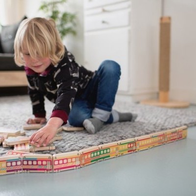 Brinquedo de comboio de madeira colorido em chão claro com criança a brincar na sala