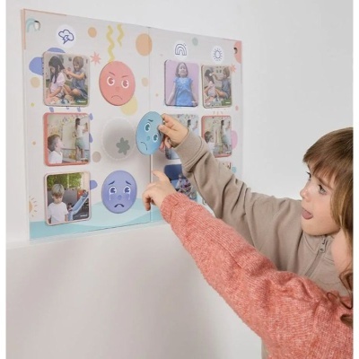 Crianças a interagir com livro infantil ilustrado com emojis coloridos e fotos.