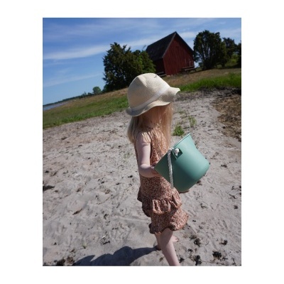 Menina com chapéu branco e vestido floral a segurar balde azul claro na praia