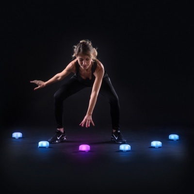 Mulher a treinar com discos LED coloridos no chão, fundo preto