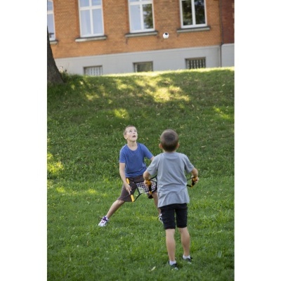 Duas crianças a jogar com raquetes de plástico e uma bola num campo de relva