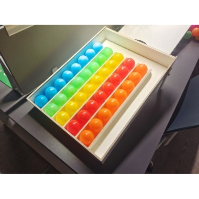 Caixa de madeira com bolas plásticas coloridas organizadas em filas por cores.