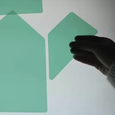 Mão segurando folha verde em formato de casa sobre superfície branca