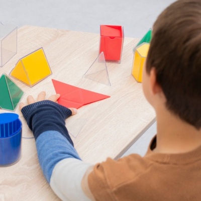 Criança manipulando formas geométricas coloridas em mesa de madeira