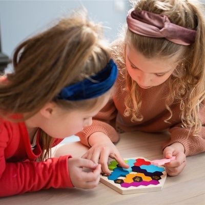 Crianças a jogar com tabuleiro de madeira hexagonal e peças coloridas