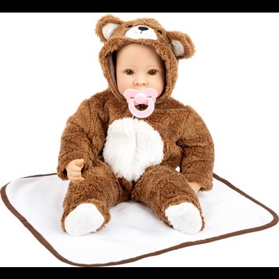 Boneca bebé com fato de urso felpudo castanho e branco sentada sobre cobertor branco com bordas castanhas