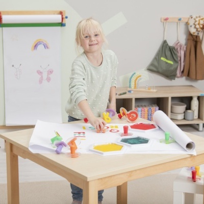 Criança a carimbar letras coloridas numa mesa com tintas e papel branco num quarto de brincadeira