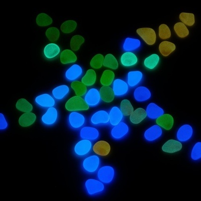 Pedras decorativas fosforescentes azuis, verdes e amarelas sobre fundo preto