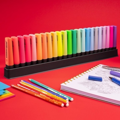 Marcadores coloridos em suporte, lápis de cor e caderno de desenho sobre fundo vermelho