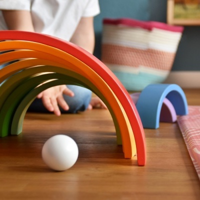 Arcos de madeira coloridos empilhados e uma bola branca em chão de madeira