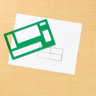 Estêncil verde com formas geométricas sobre papel branco com desenho a lápis, em mesa de madeira clara