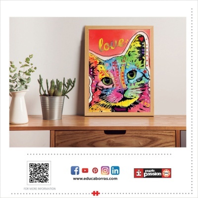 Quadro colorido de gato com a palavra love e plantas à esquerda numa mesa de madeira