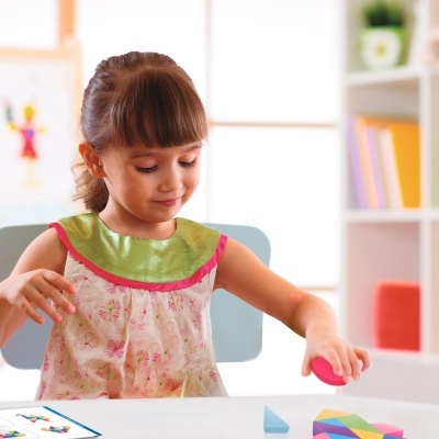 Criança em vestido floral brinca com peças de madeira coloridas numa mesa branca