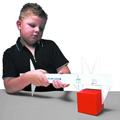 Criança mede cubo vermelho com instrumento branco em fundo branco.